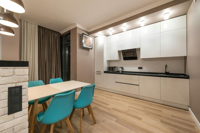 Interior of design of spacious furnished kitchen with beige walls and laminated floor and dining zone with wooden table and blue chairs