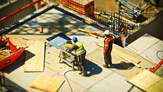 Construction workers engaging in tasks at an outdoor building site with safety hats and equipment.